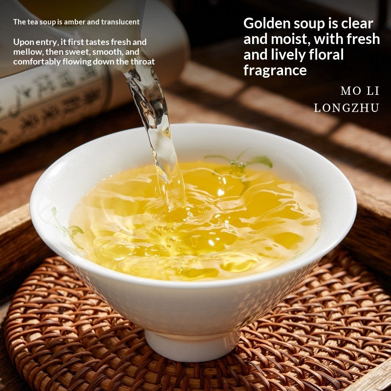 A white ceramic tea bowl filled with golden amber tea, with tea being poured into it from a metal pour-over spout. The bowl sits on a woven brown placemat on a wooden table, with a blurred teapot in the background.