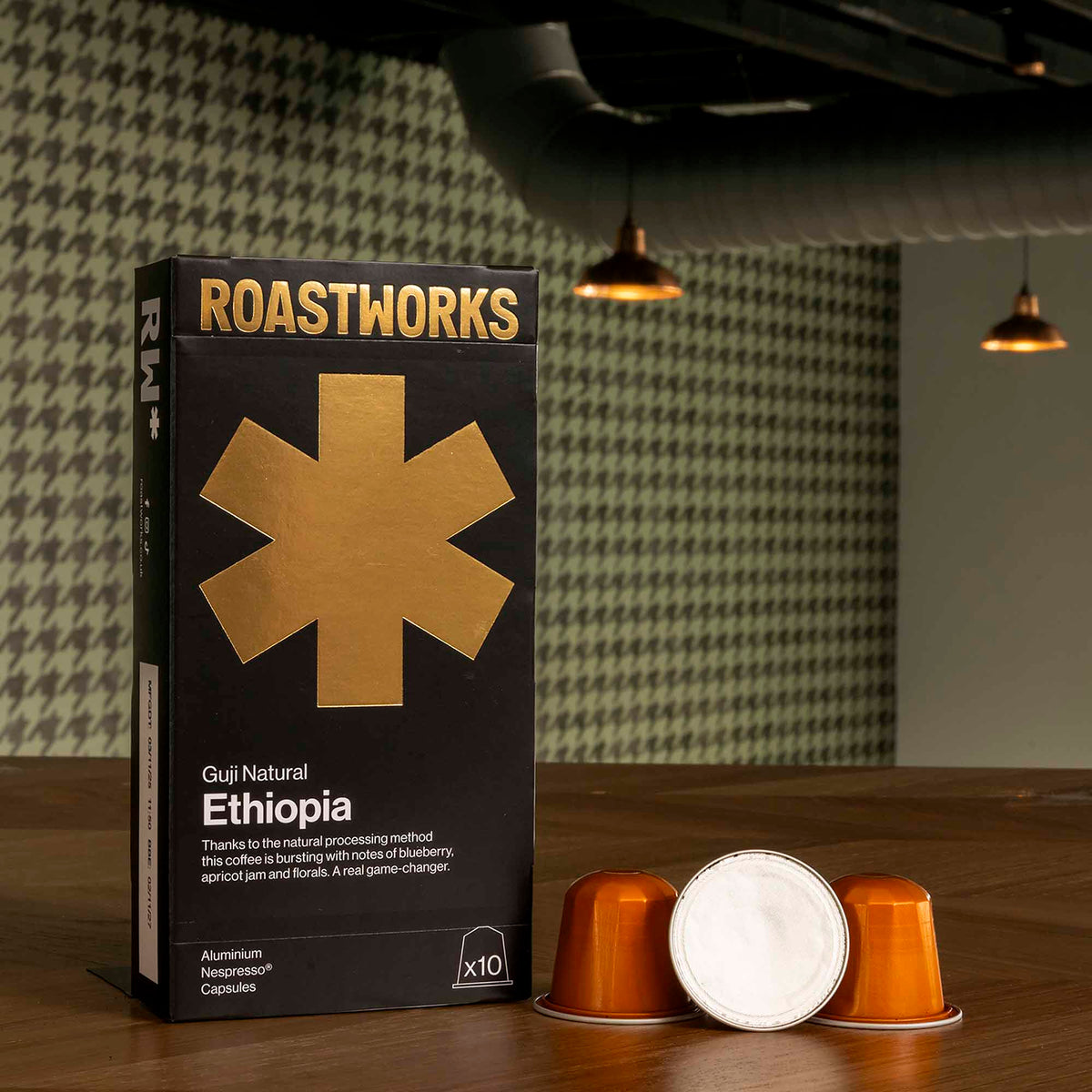 Roastworks coffee capsule packaging on a wooden surface with a blurred background